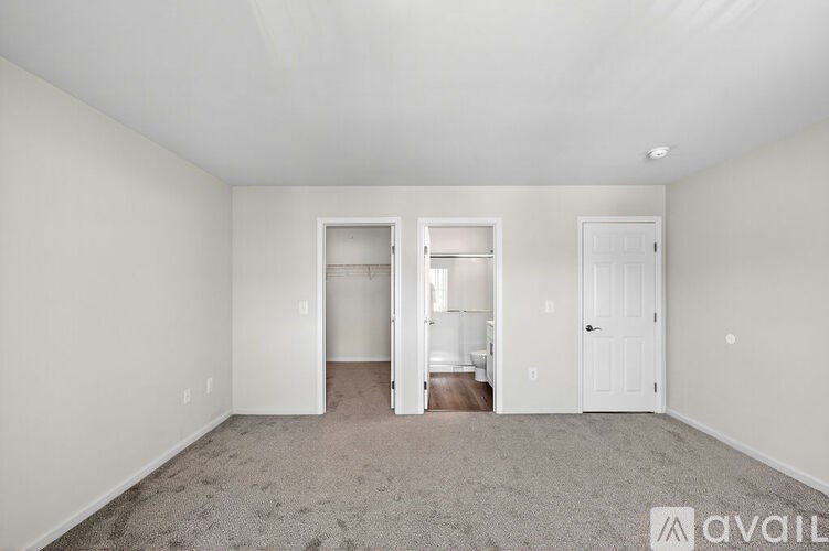 A room with a carpeted floor and white walls, with a doorway leading to another room.
