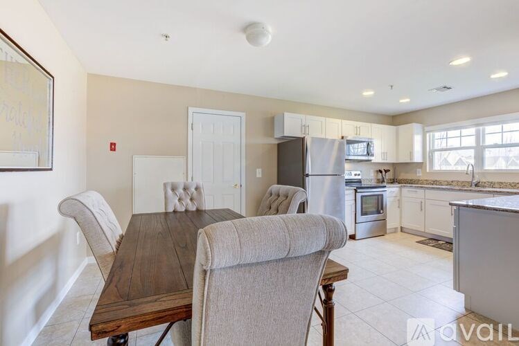 A kitchen with a table and chairs in the foreground and a refrigerator, oven, and microwave in the background.