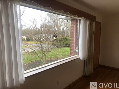 A room with a window overlooking a tree and a brick building.