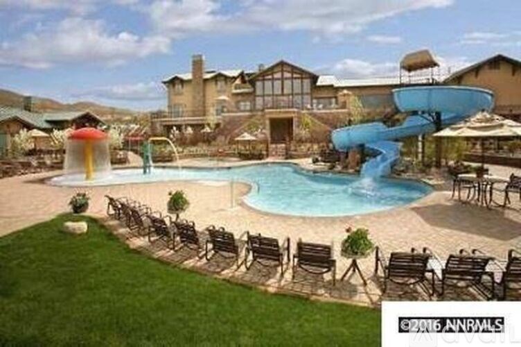 A pool with a slide and chairs around it.