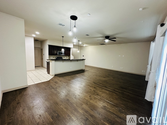 A spacious kitchen and living room with wooden floors and white walls.