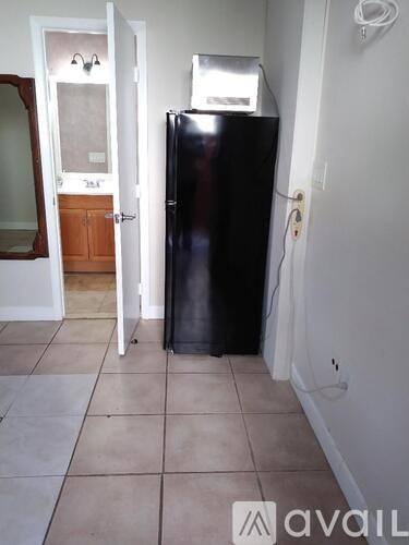 A black refrigerator in a kitchen with a white wall and a tile floor.