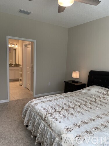 A bedroom with a bed, a ceiling fan, and a nightstand with a lamp.