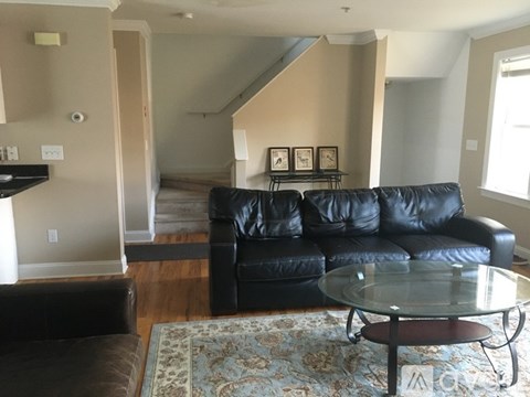 A black leather couch sits in a living room with a glass table in front of it.
