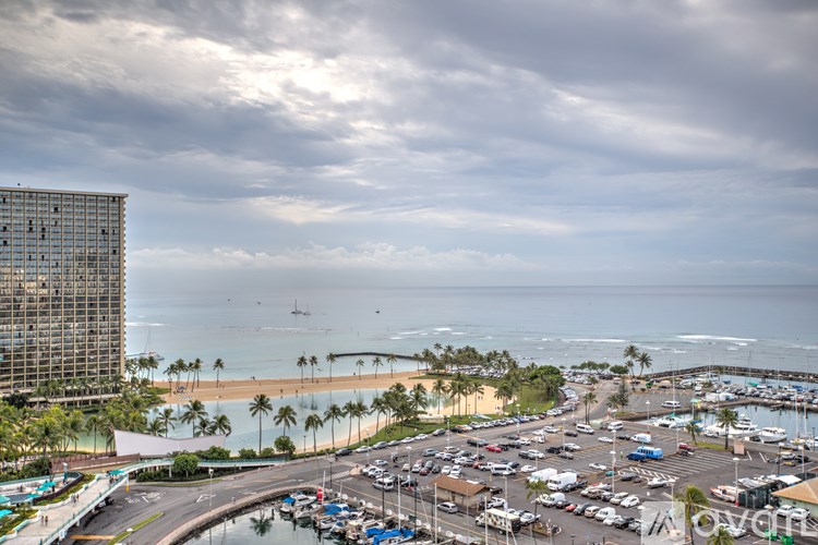 A view of a beach with a parking lot and a tall building in the background.