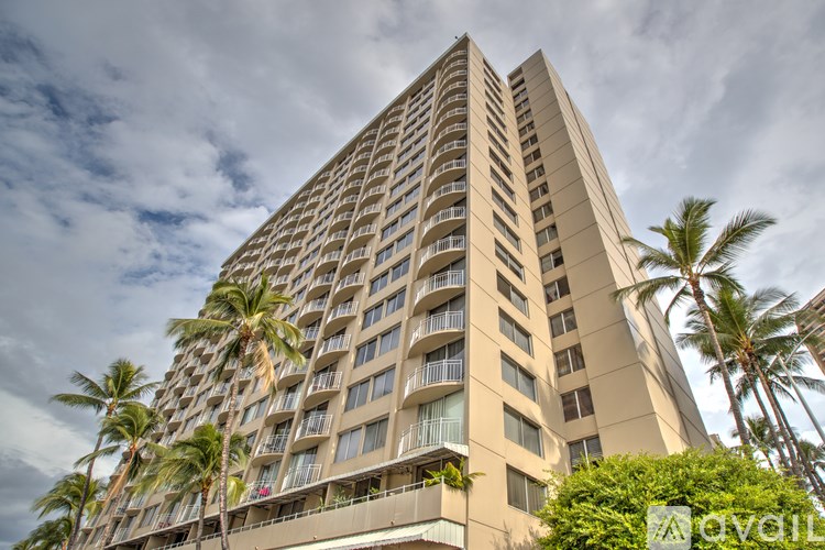 A tall building with balconies and palm trees in front.