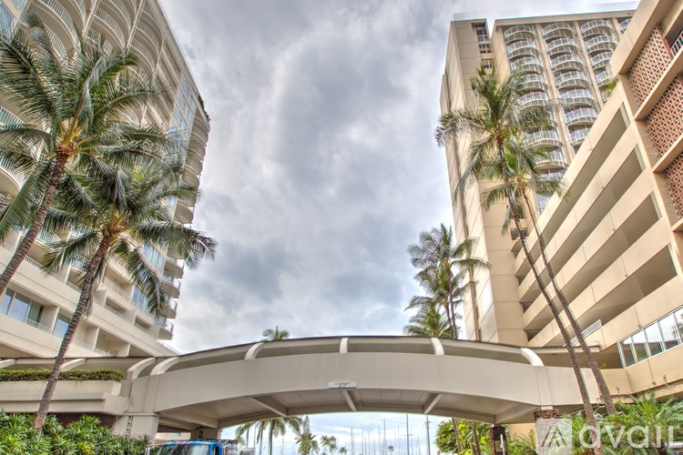 A modern building with a bridge connecting two towers with palm trees in the foreground.