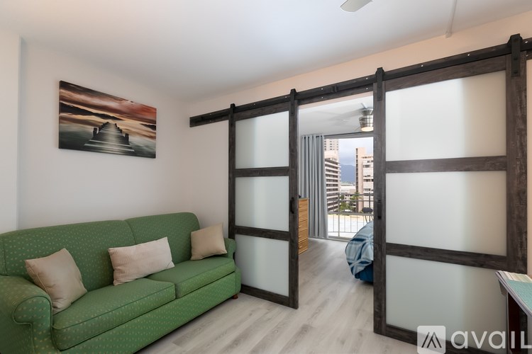 A green couch with two pillows sits in a room with a large picture on the wall and a sliding door leading to a balcony.