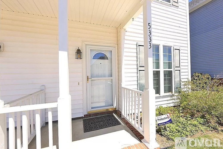 A white house with a black mat on the porch.
