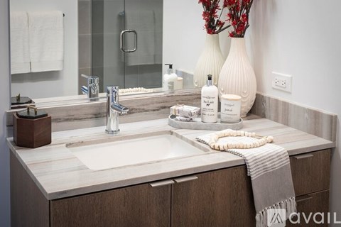 A bathroom with a sink, mirror, and a white vase with red flowers.