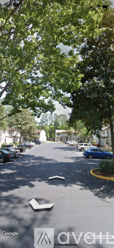 A street view with cars parked on the side and trees lining the road.