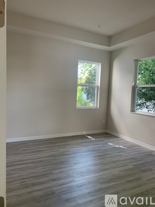 A room with wooden flooring and two windows.