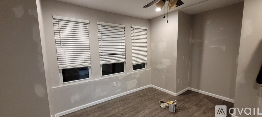 A room with a ceiling fan and three windows covered with blinds.