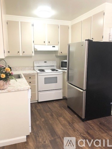 A kitchen with a black fridge, white stove and white cabinets.