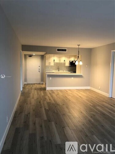 A room with wooden flooring and a kitchen area in the background.
