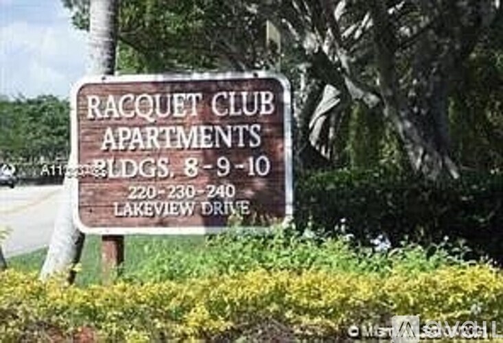 A sign for Racquet Club Apartments is shown in front of some trees.