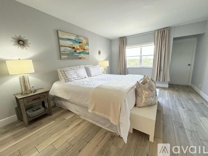 A bedroom with a large bed, a nightstand with a lamp, and a painting on the wall.