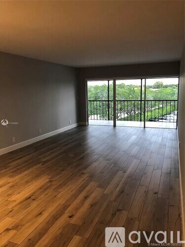 A room with wooden flooring and a view of a green outdoor area through a glass door.