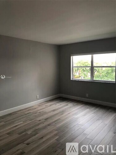 A room with wooden flooring and a window overlooking greenery.