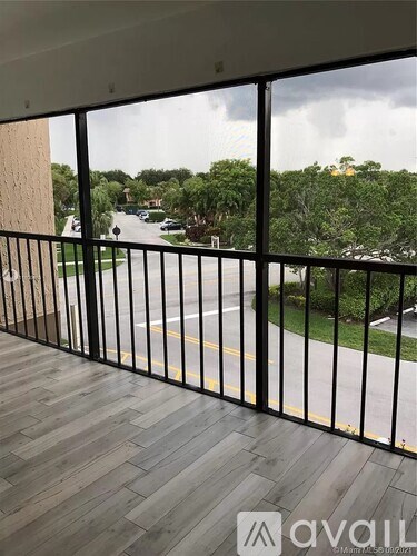 A balcony with a black railing and wooden flooring overlooks a street with cars and trees.