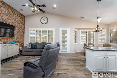 A living room with a grey chair in the foreground and a brick wall on the left side.