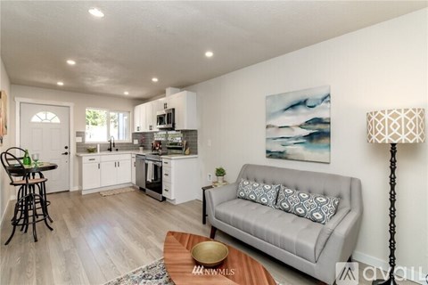 A well-lit, modern kitchen and living room with a grey sofa and a painting on the wall.