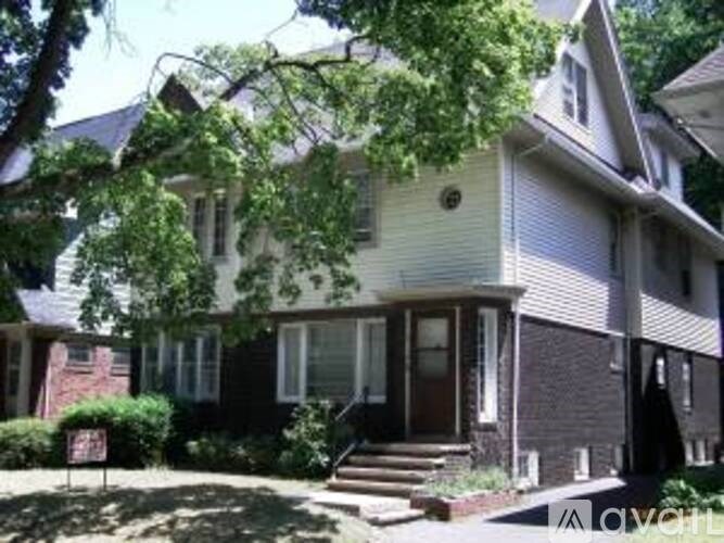 A two-story house with a front porch and a tree in front.