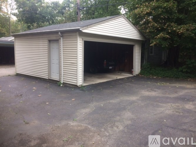 A garage with a metal roof and a white door is surrounded by trees.
