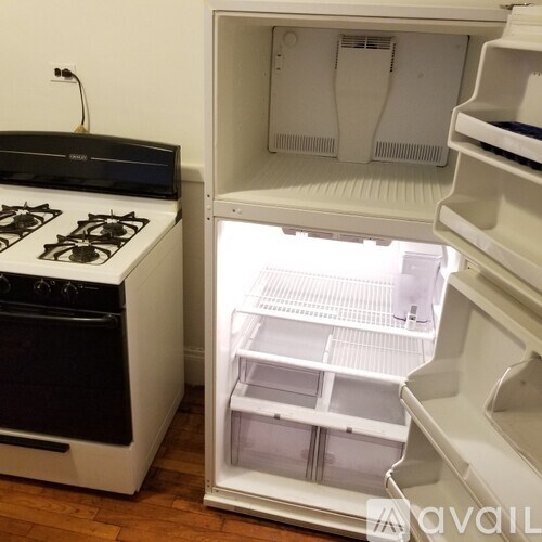 A white fridge with the door open and a black stove underneath it.