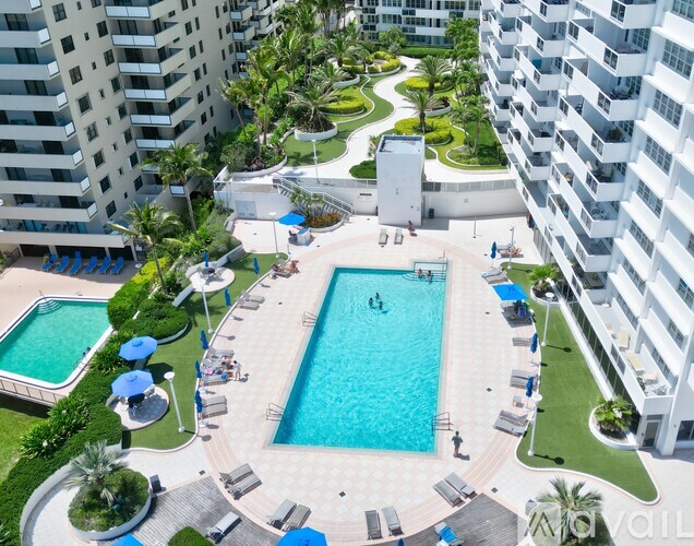 A large swimming pool surrounded by lounge chairs and umbrellas in a residential area.