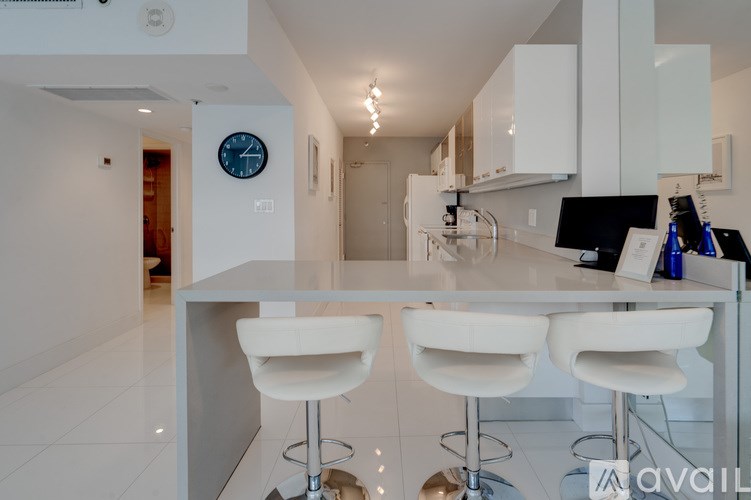 A modern kitchen with white chairs and a bar stool.