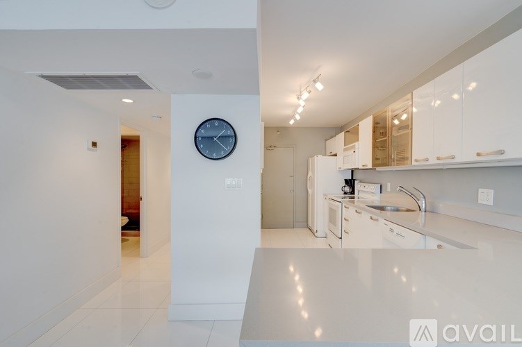 A modern kitchen with white cabinets and a clock on the wall.