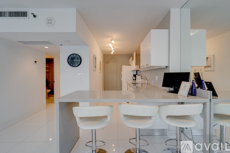 A modern kitchen with white chairs and a bar stool.