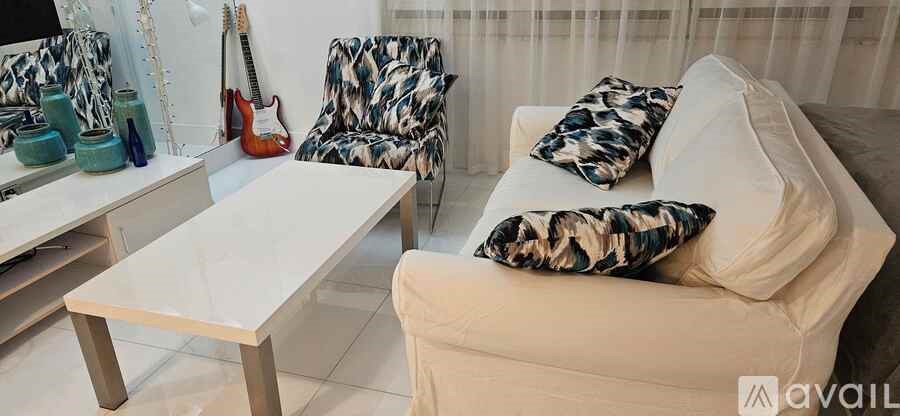 A white couch with a guitar and two vases on a table.