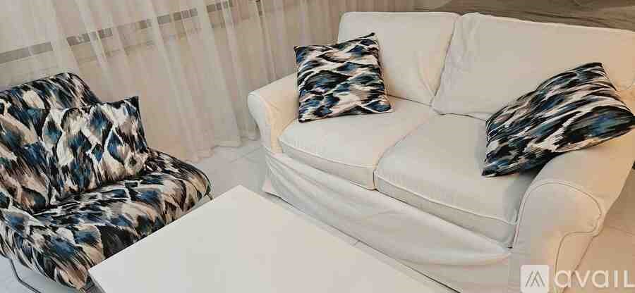 A white couch with two patterned pillows and a matching ottoman.