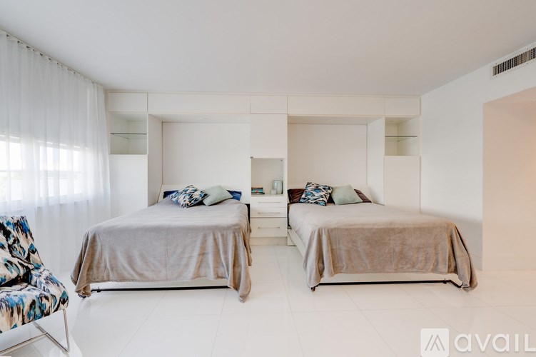 Two beds in a white room with a chair and a window with curtains.