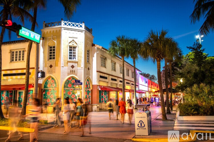A busy street scene with people walking and palm trees lining the sidewalk.