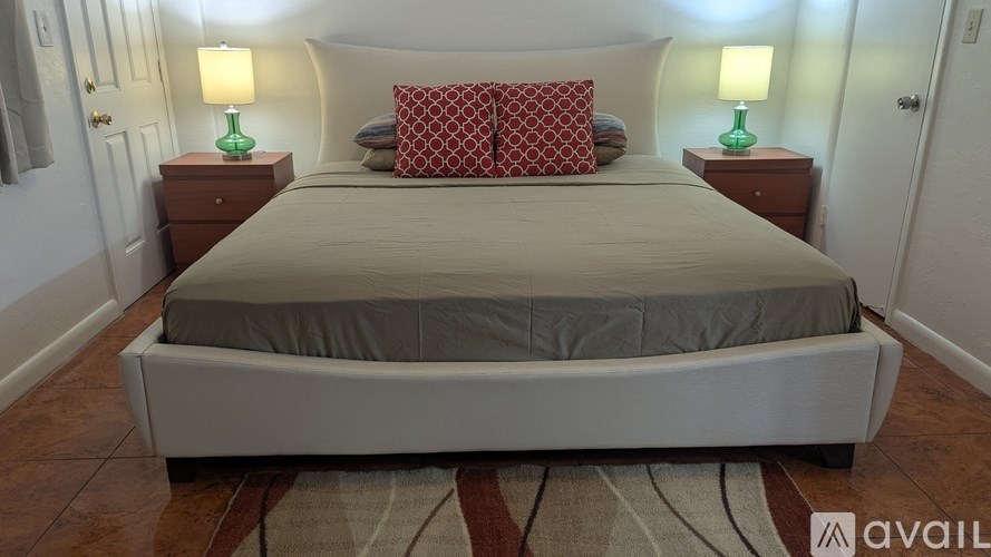 A bed with a grey sheet and two red pillows with a lamp on each side.