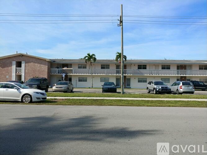 A street view of a residential area with cars parked and a building in the background.