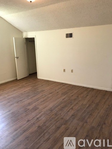 A room with wooden flooring and a white wall with a door and a window.
