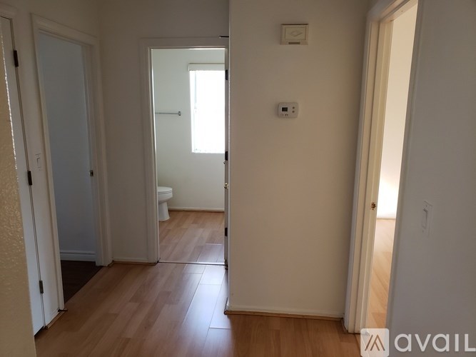 A room with wooden floors and white walls, with a door on the left and a window on the right.
