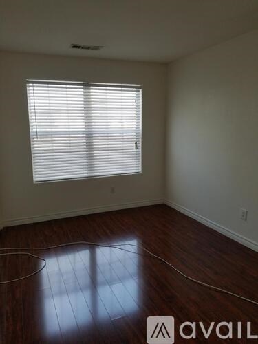 A room with a window covered by white blinds and wooden flooring.