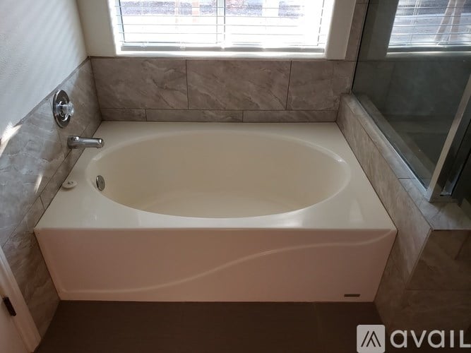 A white bathtub with a silver faucet is in a bathroom with a window.
