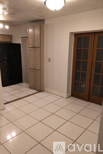 A kitchen with a black fridge, wooden cabinetry, and a tiled floor.