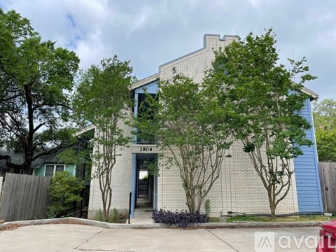 A house numbered 1904 is surrounded by greenery and has a blue door.
