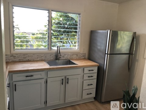 A kitchen with a stainless steel refrigerator and a window with blinds.