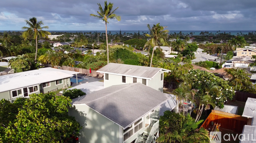 A house with a grey roof is surrounded by greenery and palm trees.