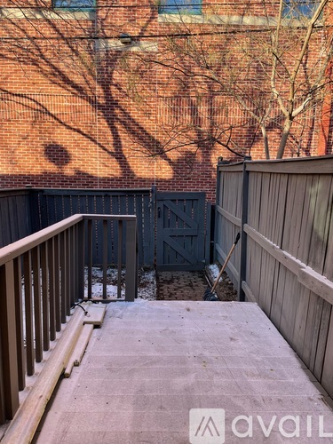 A wooden deck with a railing and a black gate in front of a brick building.