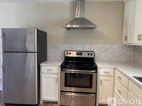 A kitchen with a stainless steel refrigerator, a stove with an oven, and white cabinets.
