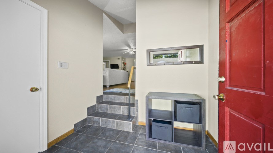 A hallway with a red door and a staircase with a grey railing.